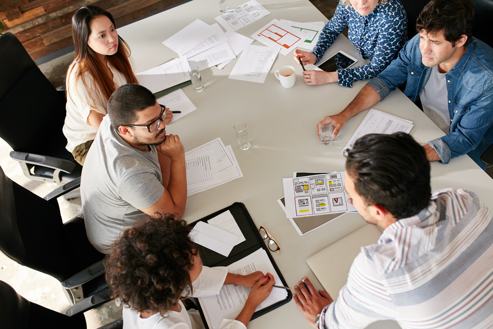 High angle view of creative team sitting around table discussing business ideas. Mixed race team of creative professionals meeting in conference room.